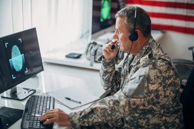 American soldier sitting in an office alone, using a computer.